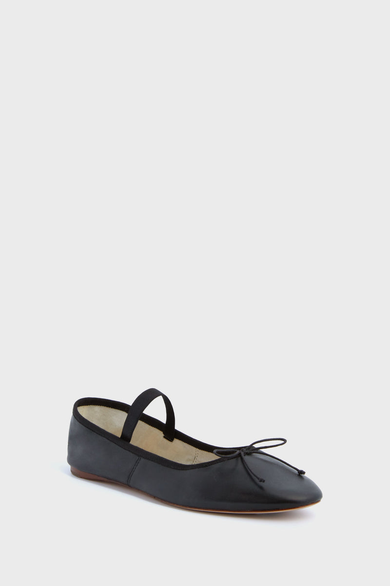 The Loeffler Randall Leonie Flat is a black leather ballet flat with a slim top strap, a delicate front bow, and a flat sole, shown against a plain white background.