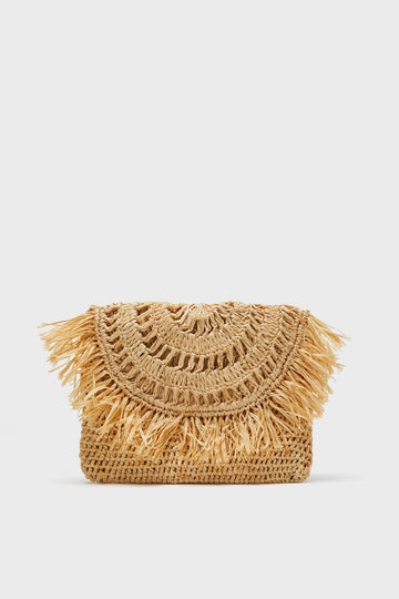 The Mar y Sol woven straw clutch features a curved flap, decorative fringe, and intricate patterns. Handmade in Madagascar using sustainable materials.