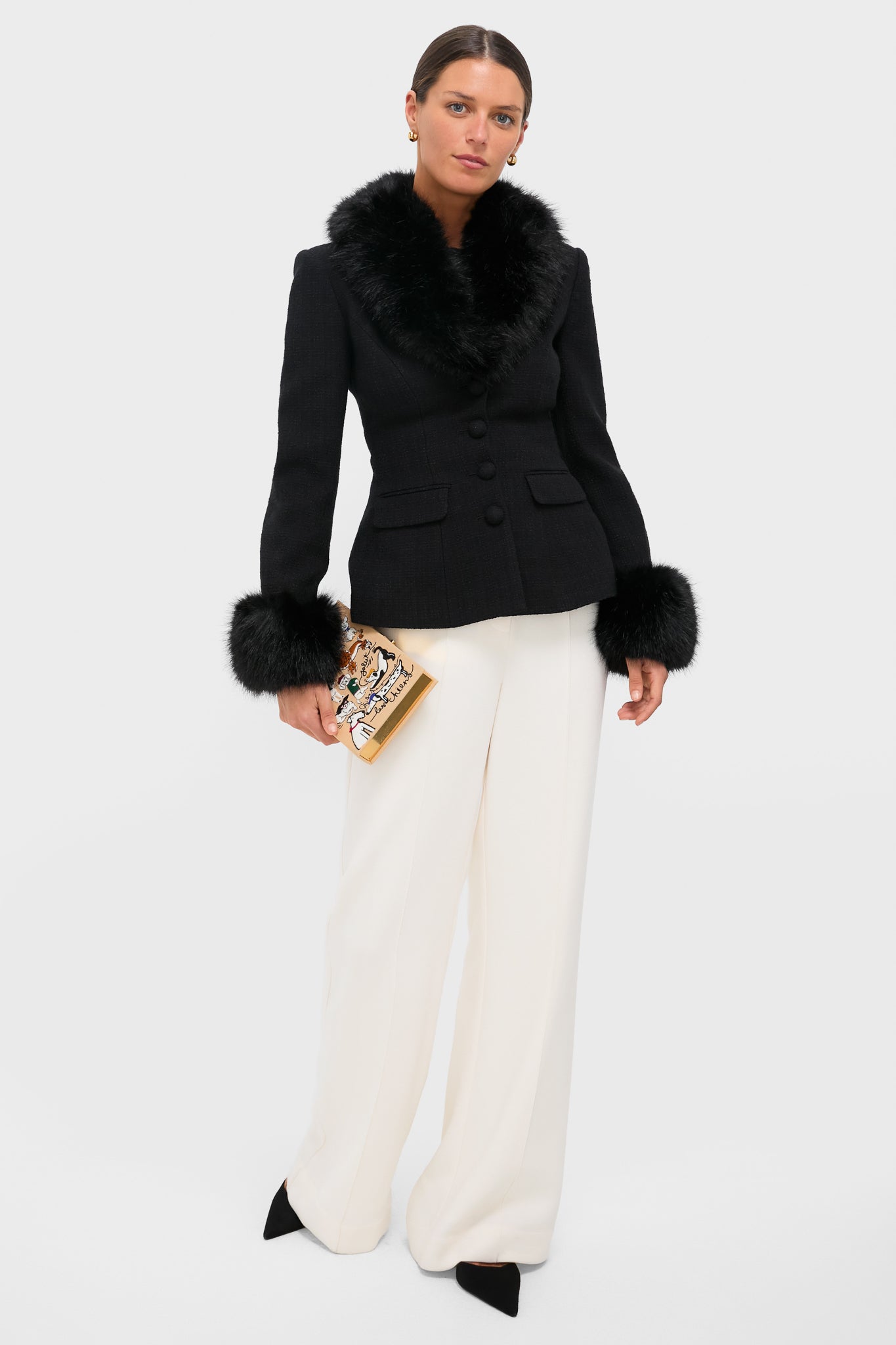 Woman in tailored jacket and wide-leg trousers holds the Latte Les Chiens Caramel Book Clutch, a classic, high-end accessory blending effortless style and fun whimsy.