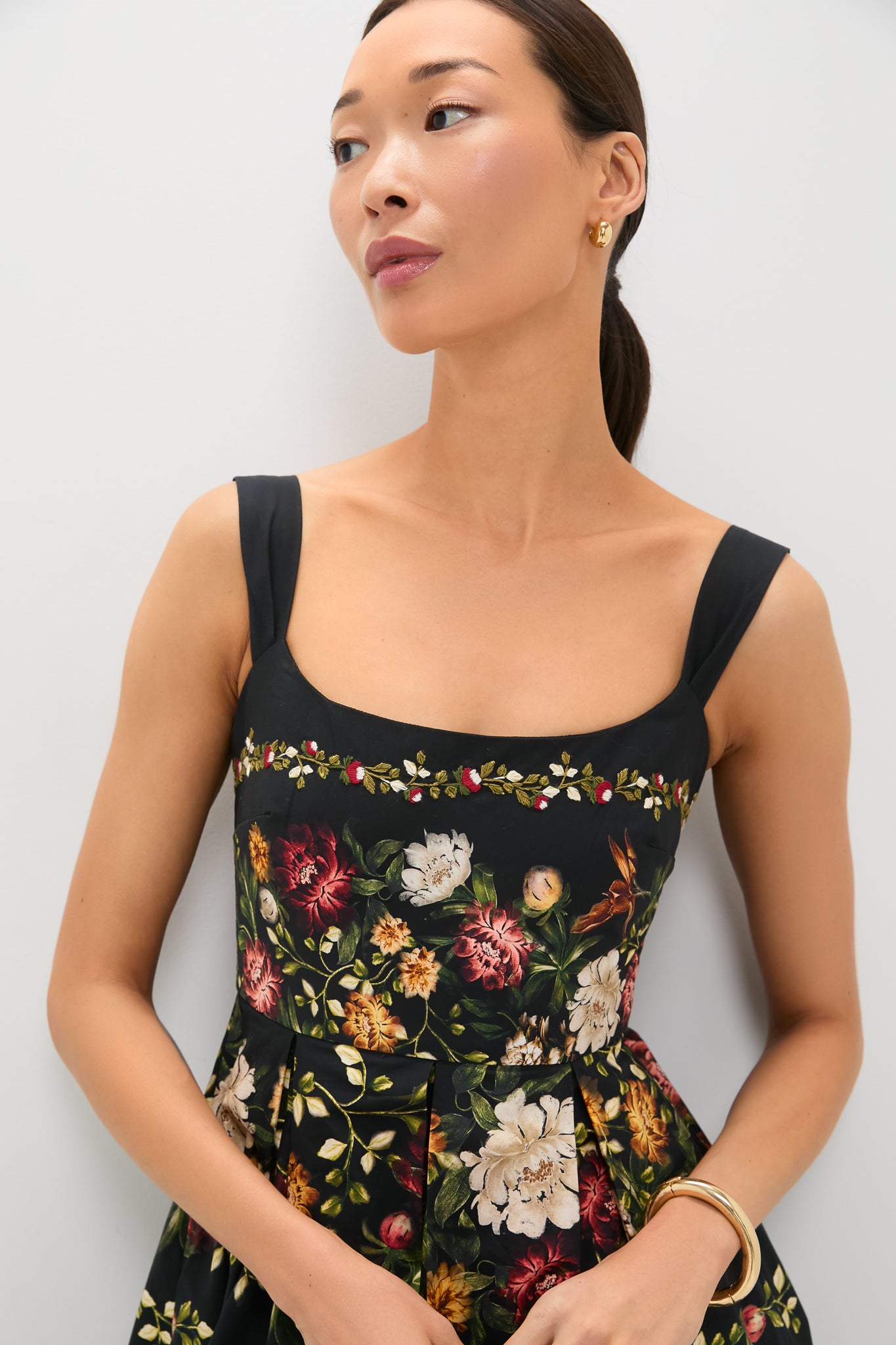 Model wearing the Paramo Alcaparra Midi Dress, a classic, sleeveless piece with bold floral prints and an embroidered vine, accessorized with gold hoops and bangle, epitomizing effortless high-end style.