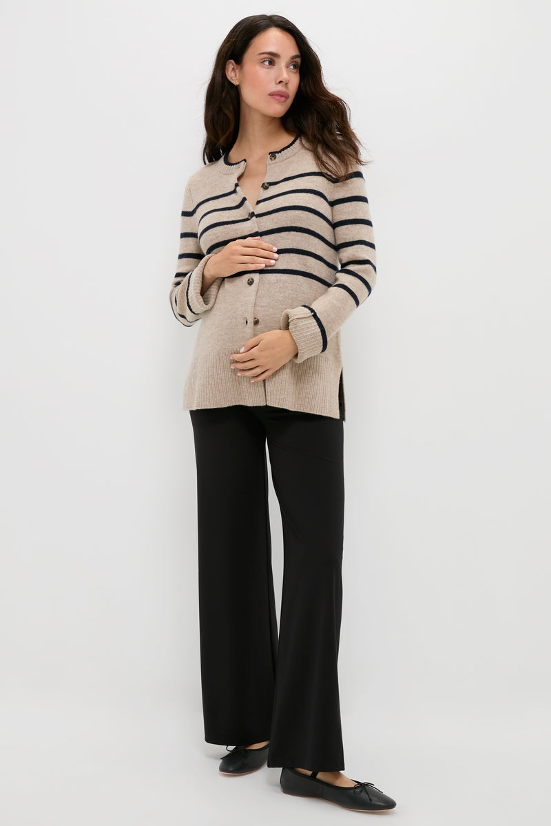 A woman stands against a plain white background, wearing a HATCH beige and black striped maternity sweater, black wide-leg pants, and black shoes, with one hand on her stomach.