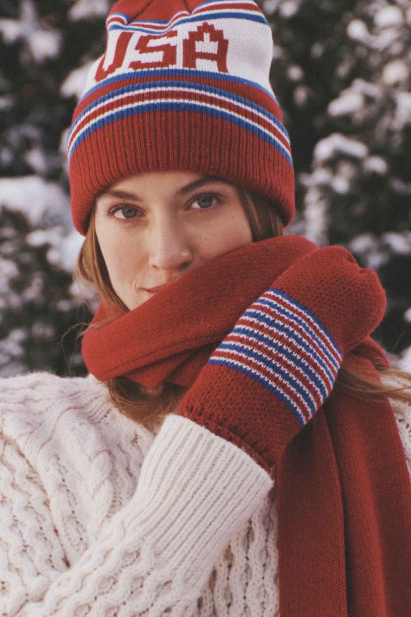 Person wearing USA Minnesota Mittens with bold stars, styled effortlessly with a matching hat and scarf, embodying classic, fun, high-end winter fashion amidst snowy evergreens.