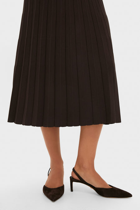 A person wearing a black STAUD midi skirt with pleats and black pointed-toe slingback heels stands against a white background.