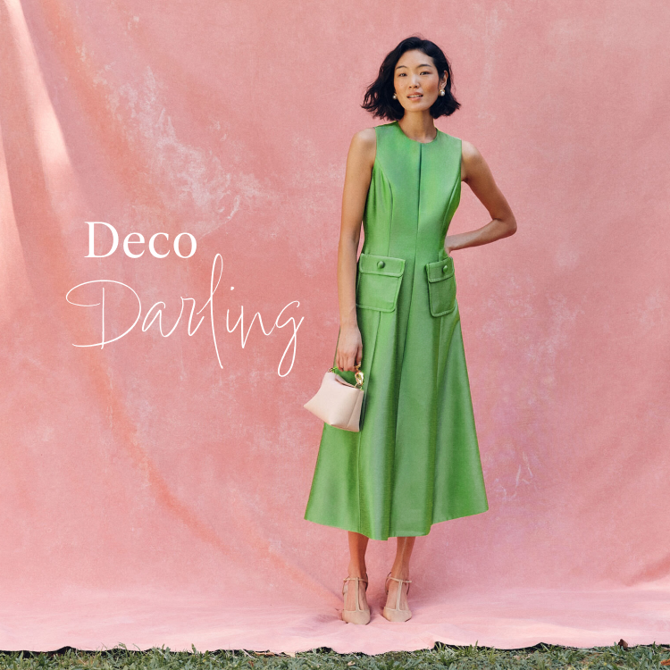 Woman in a green sleeveless midi dress standing in front of a pink background with white copy saying Deco Darling. 