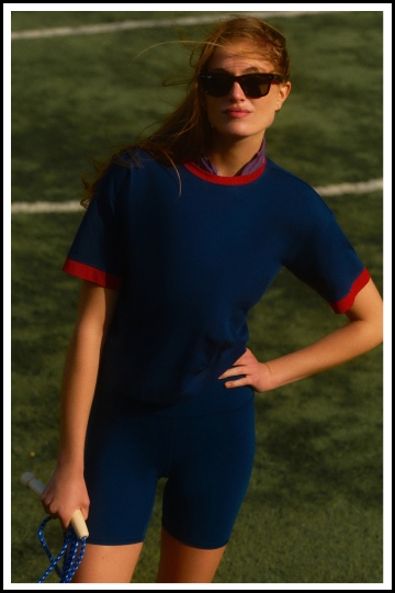 Woman standing on a field in a navy tee with red trim and navy bike shorts. 