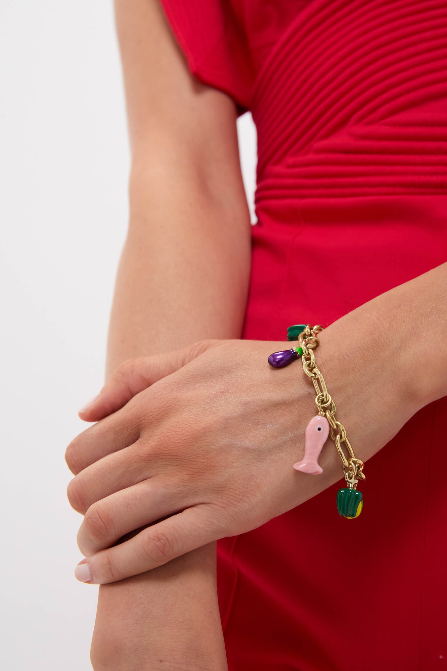 Close-up of a woman's forearm in a red dress, wearing the Multi Tesori Fish Bead Bracelet. This chunky, fun charm bracelet features classic, brightly colored enamel charms for an effortless, high-end look.