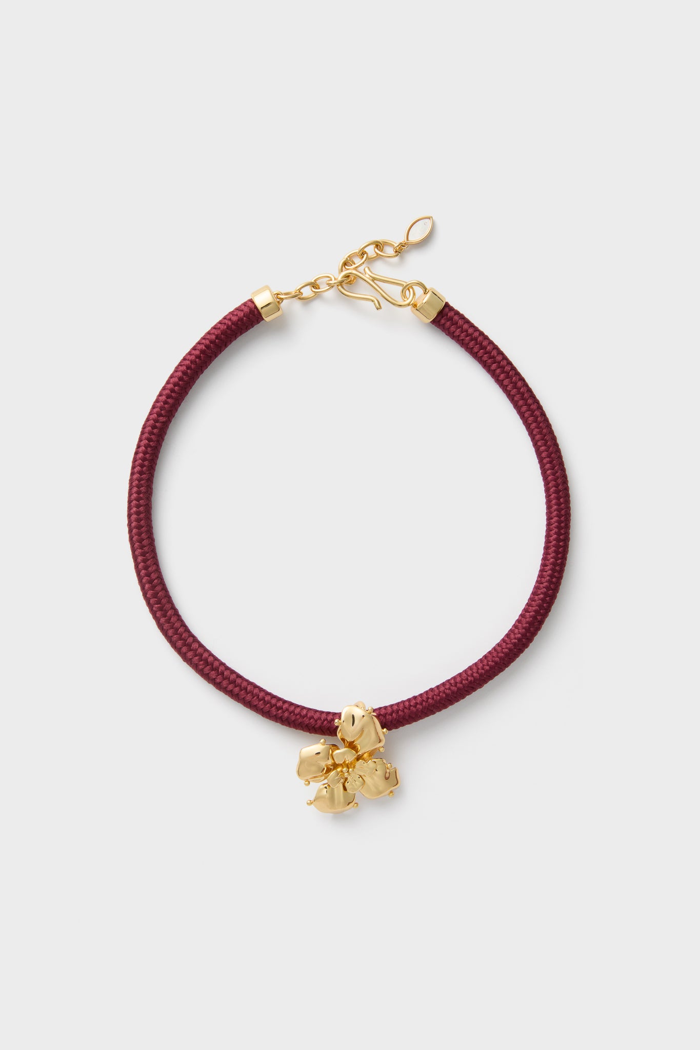 Maroon Lelani Necklace: A classic, effortless design featuring a burgundy braided cord, gold-tone fittings, and a removable gold-plated flower charm for versatile, high-end style.