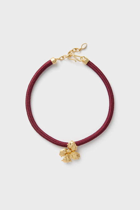Maroon Lelani Necklace: A classic, effortless design featuring a burgundy braided cord, gold-tone fittings, and a removable gold-plated flower charm for versatile, high-end style.