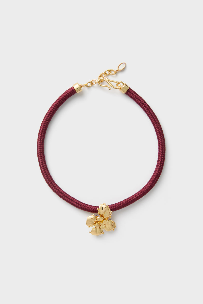 Maroon Lelani Necklace: A classic, effortless design featuring a burgundy braided cord, gold-tone fittings, and a removable gold-plated flower charm for versatile, high-end style.