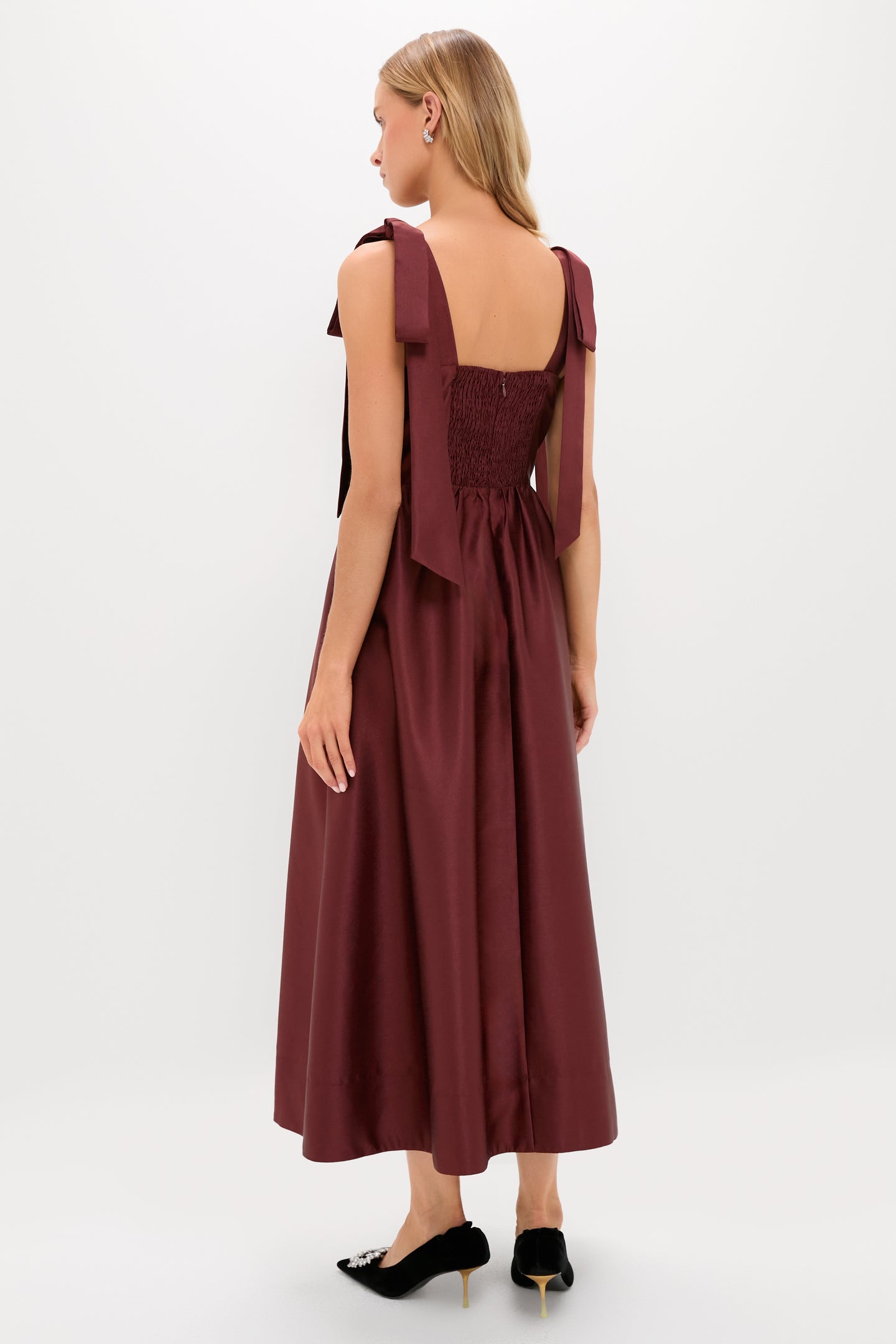 Woman in an Oxblood Dupioni Bow Esme Dress with wide shoulder bows, fitted shirred bodice, and full skirt, embodying classic elegance and effortless style.