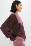 A woman in profile wears an Isabel Marant Etoile chunky, color-blocked maroon and pink patchwork cable-knit sweater with matching pink corduroy pants against a plain white background.