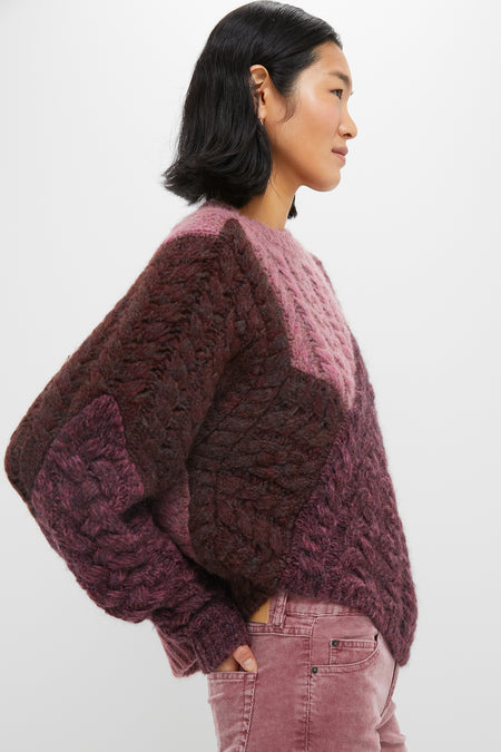 A woman in profile wears an Isabel Marant Etoile chunky, color-blocked maroon and pink patchwork cable-knit sweater with matching pink corduroy pants against a plain white background.