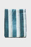 A folded Goldie Home European linen tablecloth with vertical blue and white stripes is displayed, perfect for modern table decor.
