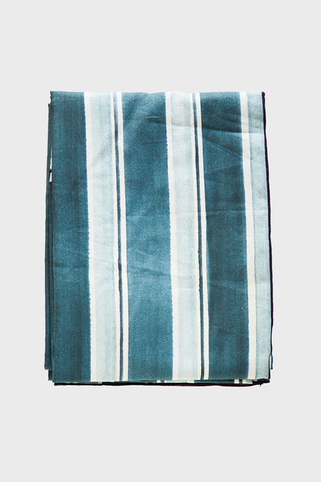 A folded Goldie Home European linen tablecloth with vertical blue and white stripes is displayed, perfect for modern table decor.
