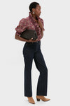 A person stands holding a black clutch, wearing a floral ruffled blouse, high-waisted dark jeans, tan boots, and elegant Lizzie Fortunato Laurel Earrings.
