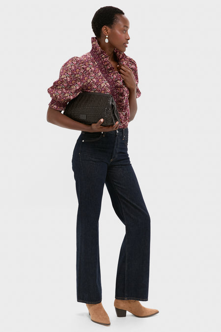 A person stands holding a black clutch, wearing a floral ruffled blouse, high-waisted dark jeans, tan boots, and elegant Lizzie Fortunato Laurel Earrings.