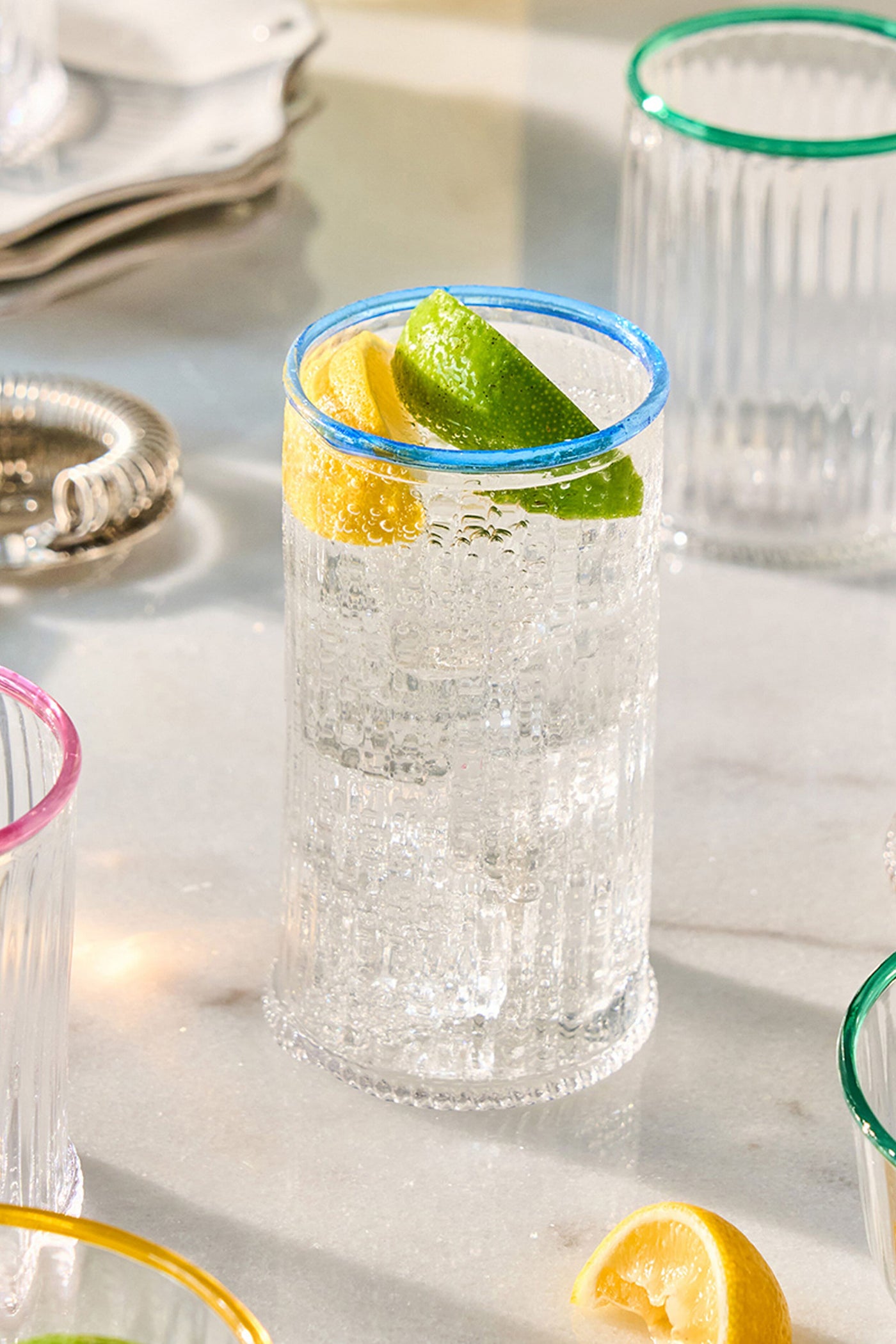 Chambray Nell Highball: A classic, effortlessly chic ribbed glass with a fun blue rim, filled with sparkling water and citrus, exuding high-end elegance.