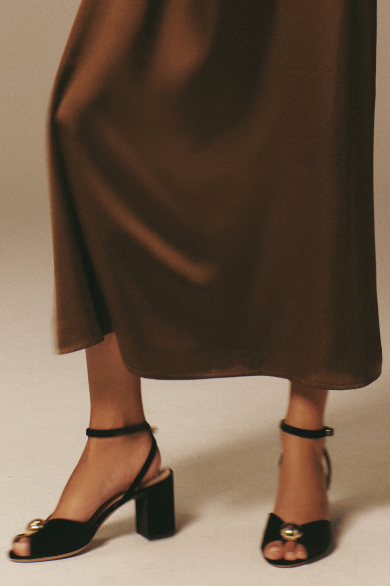 The Black Velvet Jewel Heel features a classic design with a gold ornament, block heel, and ankle strap, embodying effortless elegance for a high-end, fun style.