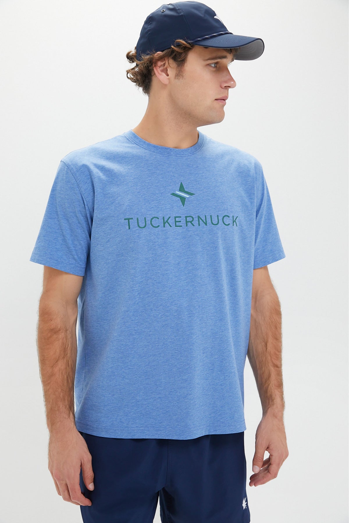 A man in a Nautilus Blue Peter Millar Tuckernuck Tee with UPF 50+ sun protection, navy shorts, and a navy cap looks to his right.