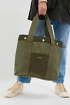 Person holding the classic Olive Healy Tote Bag, featuring effortless quilted design, corduroy pocket with Barbour logo, and high-end webbed handles. Perfect for fun, everyday use.