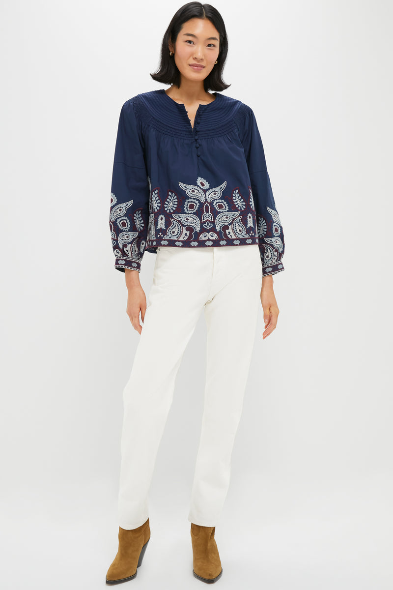 Woman wearing classic Navy Embroidered Lucia Blouse with pintuck yoke and paisley border, paired with high-rise white pants and tan suede ankle boots; an effortless, high-end style.