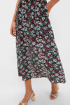 Someone wears a Ciao Lucia floral slip maxi dress featuring red, white, and blue flowers. The long, dark dress is paired with beige heeled sandals. The image is cropped at the shoulders.