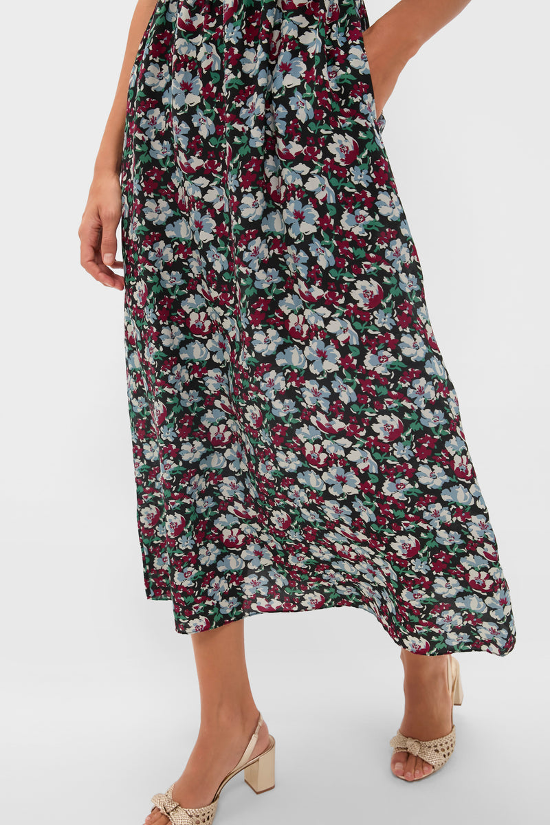 Someone wears a Ciao Lucia floral slip maxi dress featuring red, white, and blue flowers. The long, dark dress is paired with beige heeled sandals. The image is cropped at the shoulders.