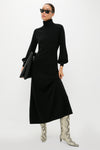 Model in a classic Black Cashmere Turtleneck Maxi Dress, featuring blouson sleeves. Paired with effortless snakeskin boots and sunglasses, exuding a fun, high-end style.