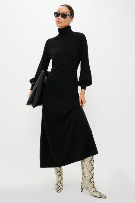 Model in a classic Black Cashmere Turtleneck Maxi Dress, featuring blouson sleeves. Paired with effortless snakeskin boots and sunglasses, exuding a fun, high-end style.