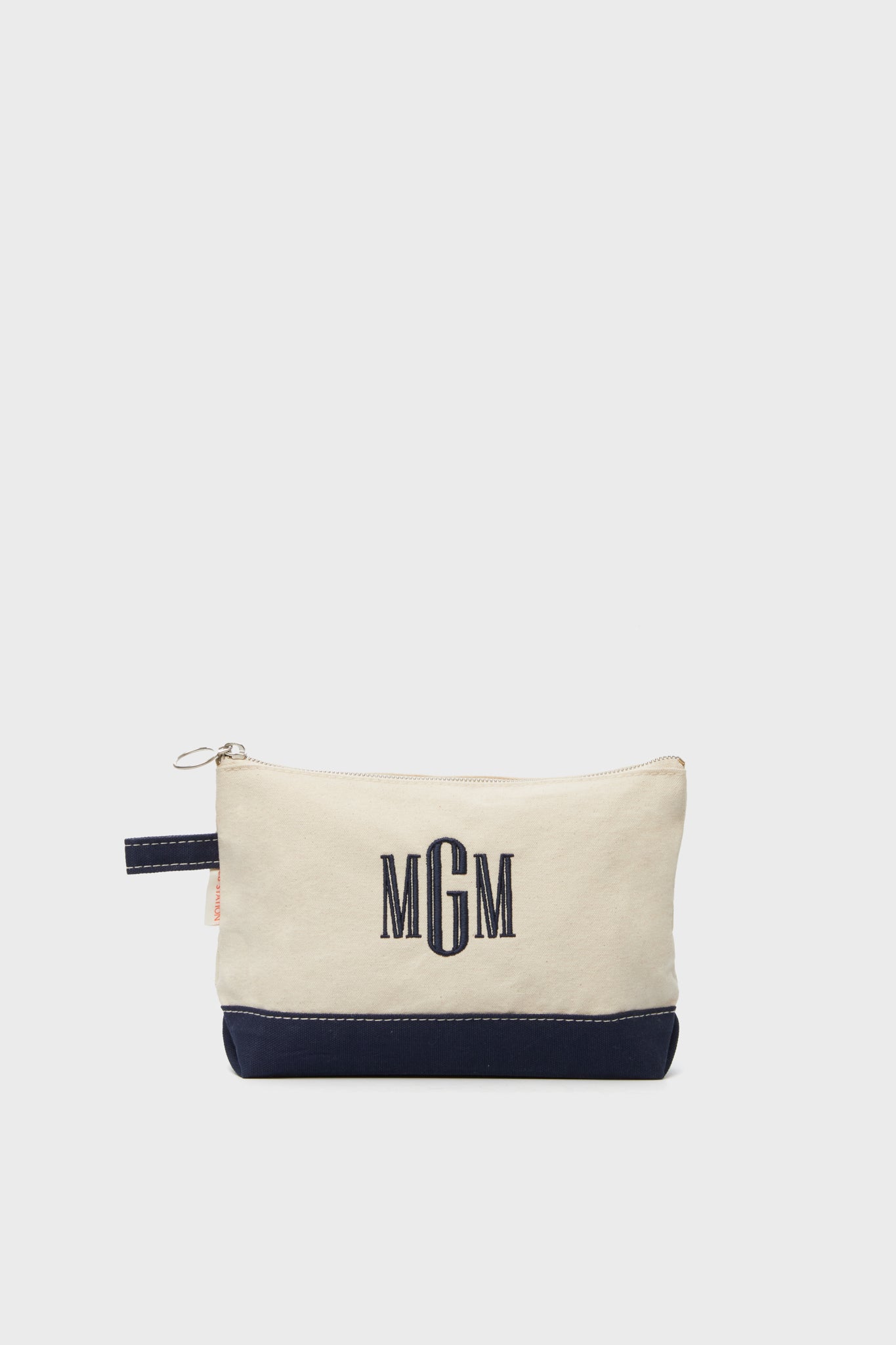 The CB Station beige cotton canvas zippered pouch features a navy base and MGM monogram embroidered in navy thread, making this makeup bag a stylish travel essential.
