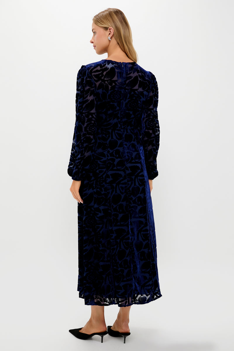 Woman in a classic Navy Burnout Velvet Odette Maxi Dress with floral pattern, long blouson sleeves, and fitted waist, styled with black mules.