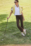 Woman in a classic, effortless look wearing Chocolate Brown 28 Inch Compression September Pant with side zip pockets, posing casually with a golf club on a grassy lawn.