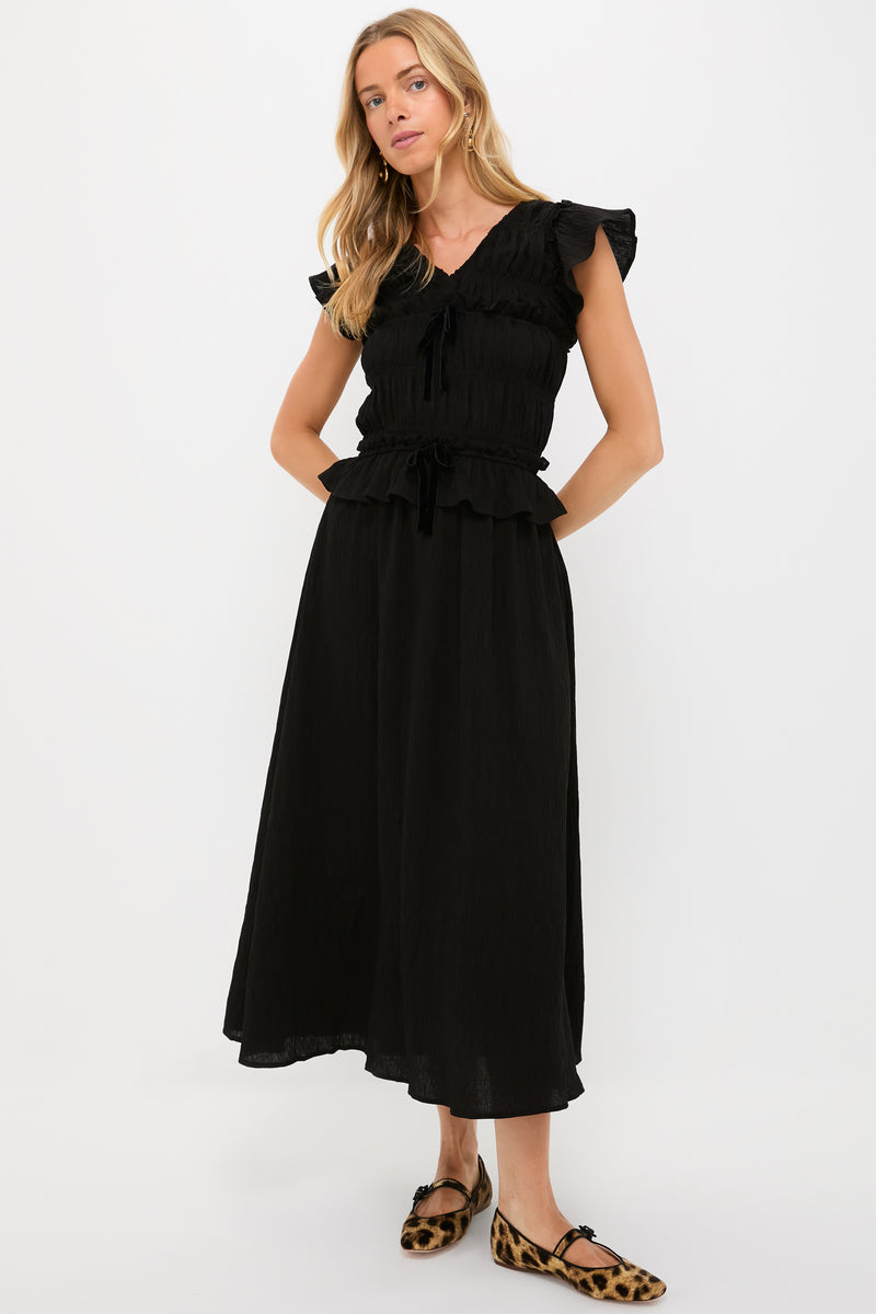 A woman wears a Moon River black ruffled maxi dress with flutter sleeves and a smocked bodice, paired with leopard-print flat shoes.
