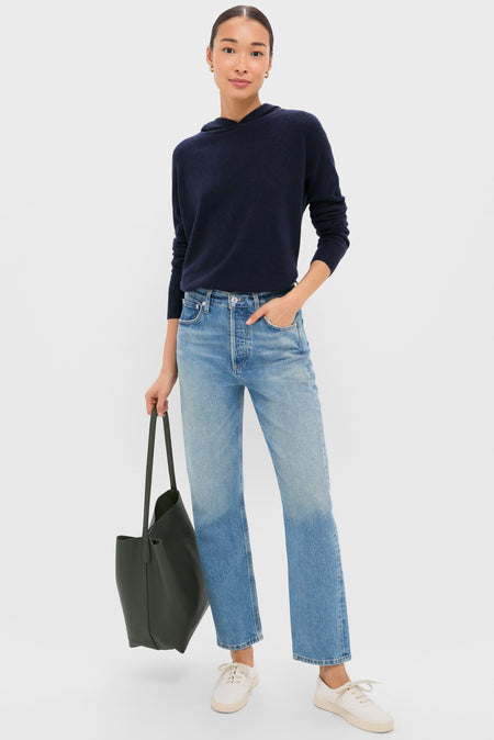 A person faces forward, wearing a Tuckernuck navy hoodie, light blue straight-leg jeans, white sneakers, and carrying a large dark green tote bag.