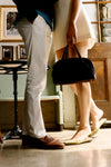 Two people standing indoors; one wears off-white trousers, the other a cream skirt, showcasing Fern Satin Nilli Flats in a classic, effortless, high-end style.