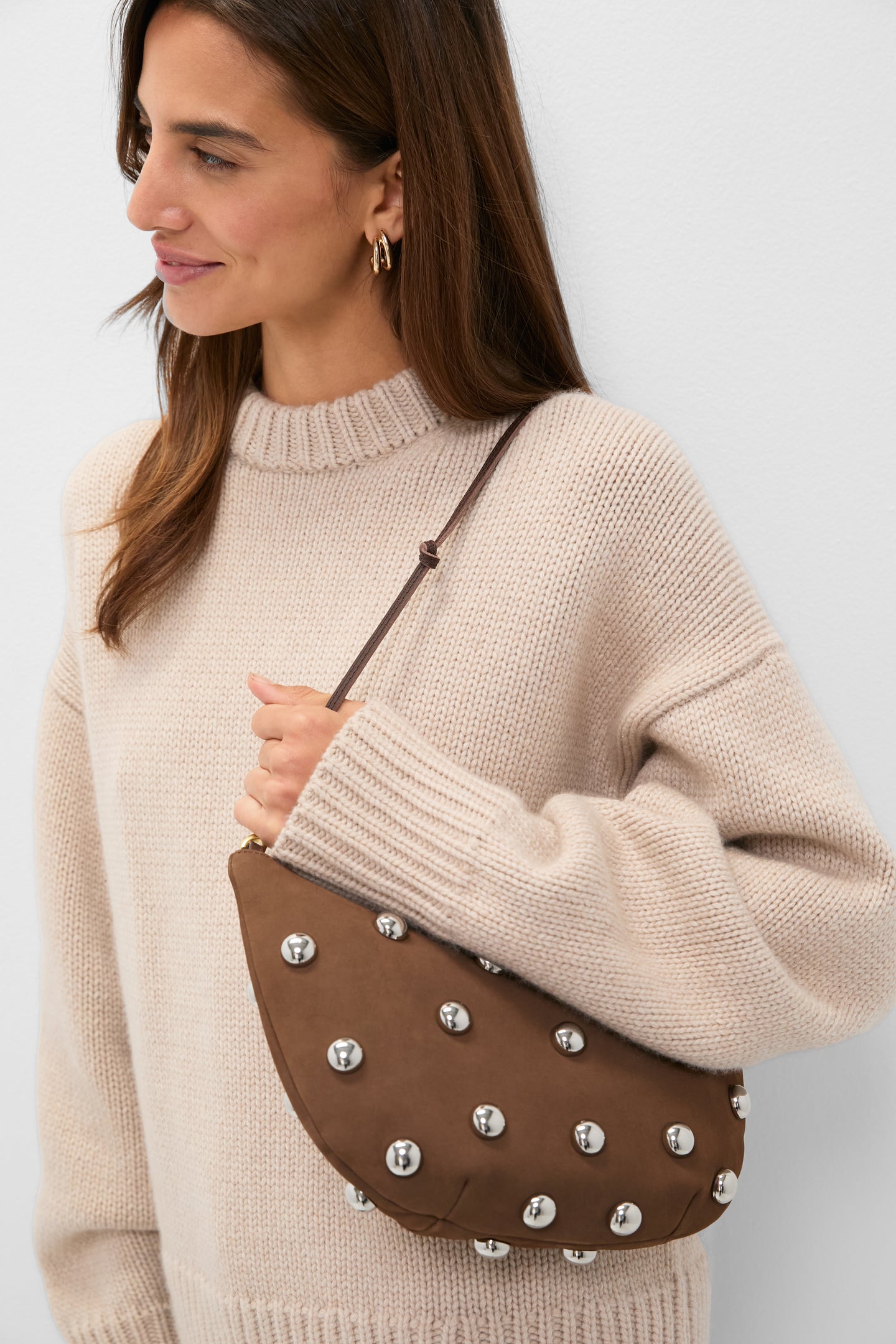 Woman holding Choco Bar Smooth Nubuck with Studs Lune Bag; classic, high-end suede crescent bag with silver studs and knotted strap, embodying effortless, fun style.