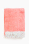 A folded Matouk coral throw made from brushed cotton, featuring white fringe trim along the edges.