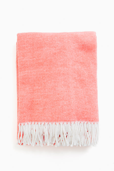 A folded Matouk coral throw made from brushed cotton, featuring white fringe trim along the edges.