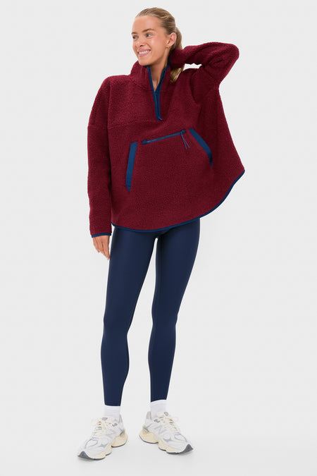 Young woman models the classic Cabernet Fleece Cady Quarter Zip, an effortless, high-end pullover with a quarter-zip and zippered kangaroo pocket, paired with navy leggings.