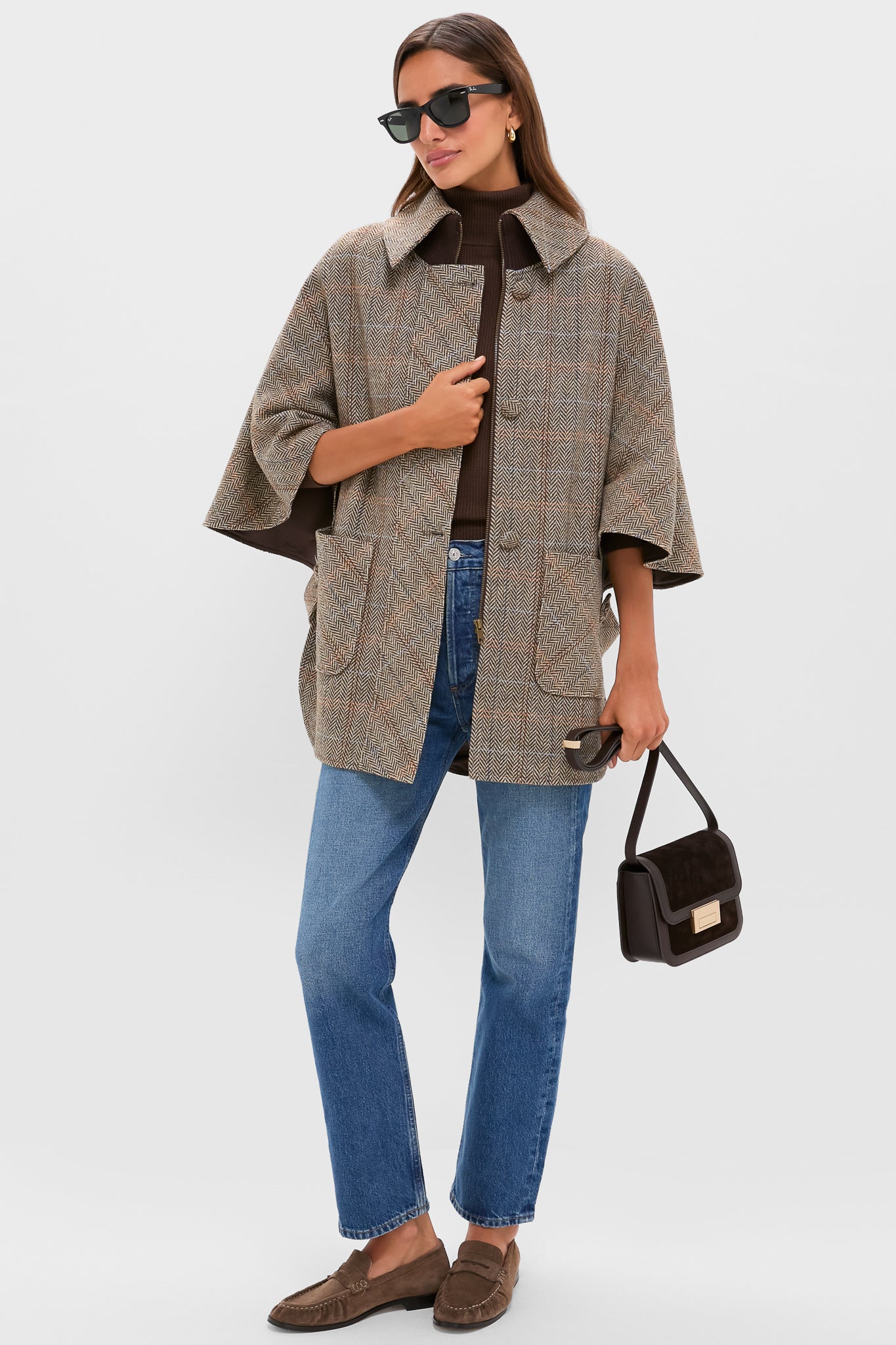 Model showcases the classic Herringbone Stewart Poncho, an effortless cape-style coat, paired with a turtleneck and jeans, epitomizing fun, high-end fall fashion.
