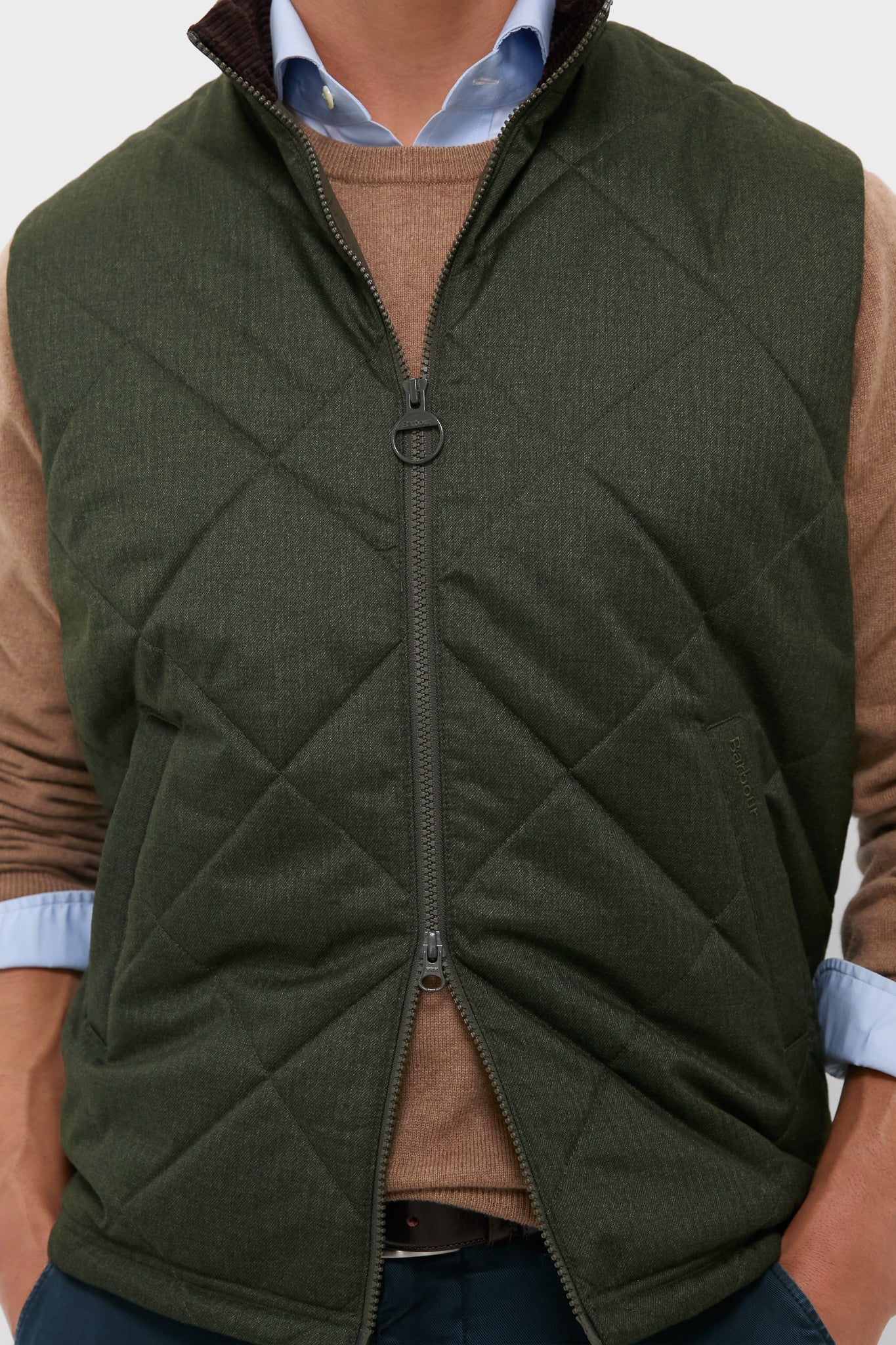 Olive Winter Finn Gilet layered over a light brown sweater and blue shirt, epitomizing classic, effortless style with high-end details for unpredictable weather.