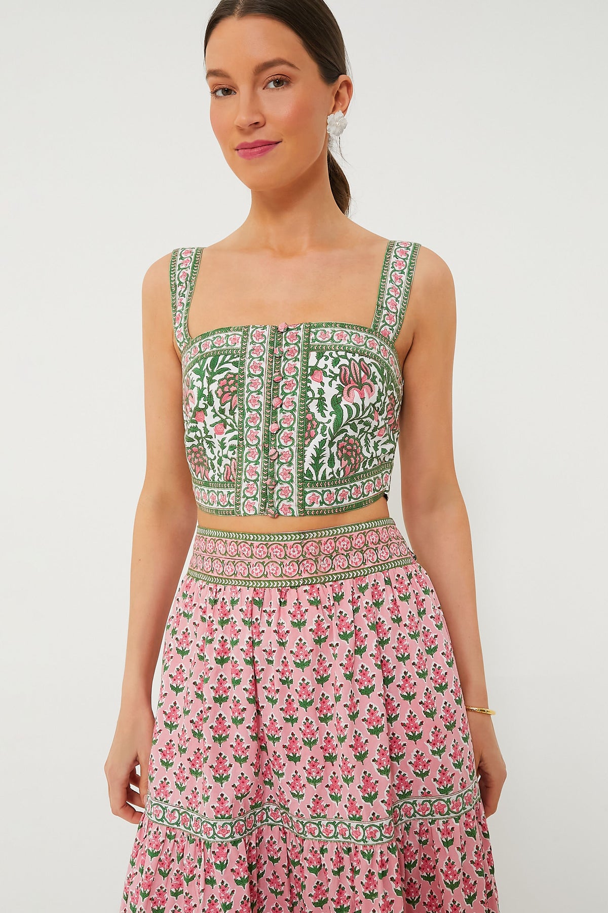 A woman showcases sustainable fashion in a Pink City Prints sleeveless, square-neck block-printed crop top and matching high-waisted skirt with green and pink floral patterns.