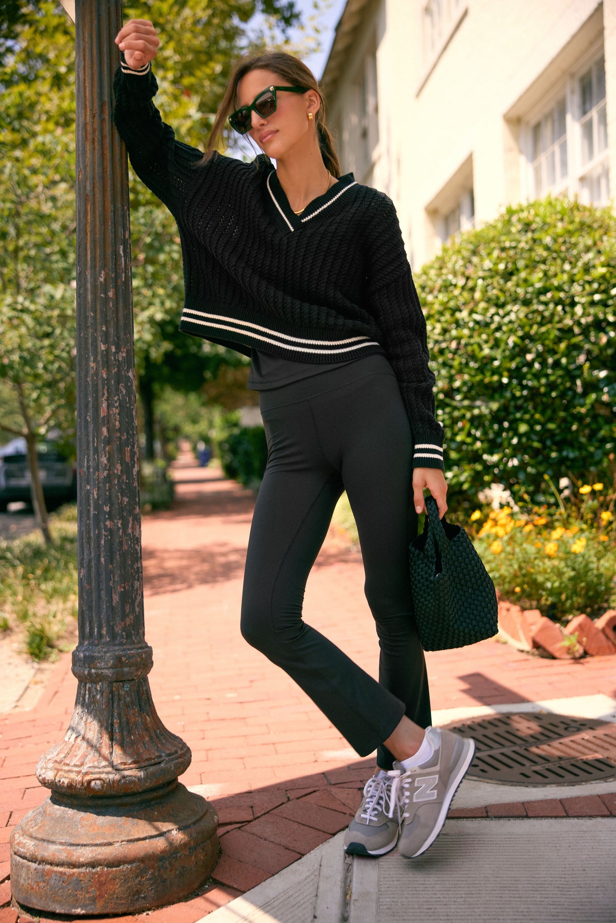 Young woman in classic, high-rise black Millie Yoga Pants, exuding effortless style with a fun, high-end vibe, leaning against a streetlamp.