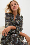 A woman in a long-sleeved, dark floral print dress by Hyacinth House sits on a chair against a plain light background, gazing directly at the camera.