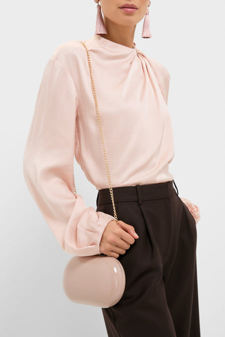 Woman holding a classic Latte Patent Selena Clutch Bag with a gold chain, complementing an effortless, high-end look featuring a soft blouse and tailored trousers.