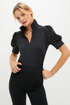 A woman confidently poses in a Tnuck Sport black women's golf shirt with short sleeves and black pants, highlighting stylish comfort and SPF protection.