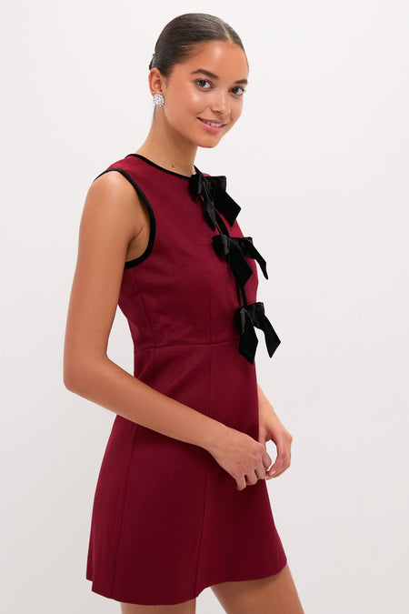Young woman in a classic Cranberry Velvet Bow Jaclyn Mini Dress, featuring black velvet bows, embodies an effortless, high-end style.