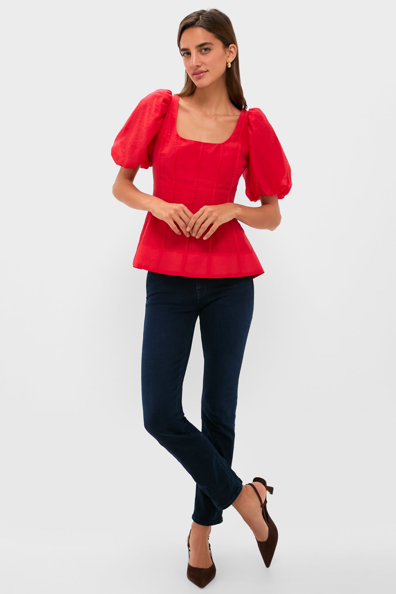 Woman in Ruby Taffeta Annalise Blouse with puff sleeves, flared hem; styled with dark skinny jeans and heels, embodying classic and effortless high-end fashion.