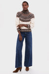 A person wears a Love the Label fair isle knit turtleneck sweater, wide-leg blue jeans, and brown heeled boots while standing against a plain white background.