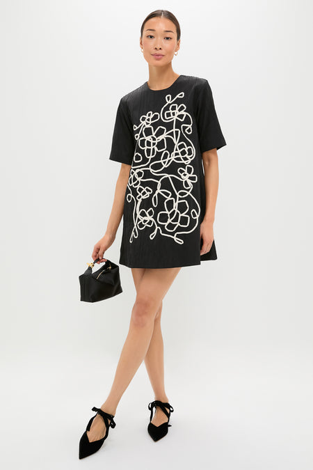 Woman in Onyx and Ivory Classic Katya Mini Dress showcasing a looping floral-vine motif, styled with ankle-tie flats and a chic handbag, exuding effortless elegance and high-end style.